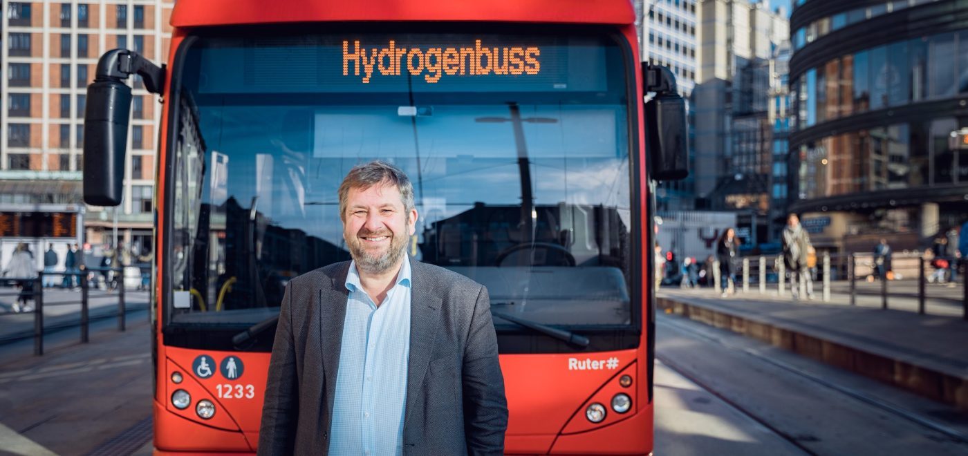 Bernt Reitan Jenssen i Ruter står foran en av de røde hydrogenbussene i Oslo sentrum.