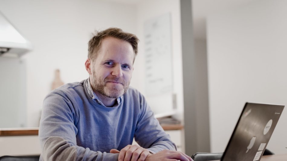 Kjell Havre Iversen sitter foran en bærbarpc på kjøkkenbordet og søker på energiportalen.no