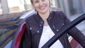 Elisabeth Sagedal, kommunikasjonssjef i Naf, står bak førerdøren i en rød bil.