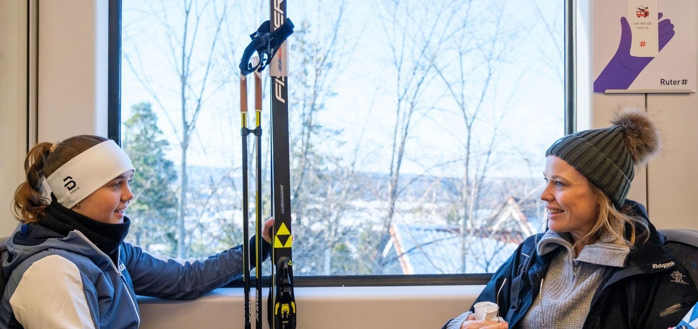 Jente og kvinne sitter på t-banen med ski