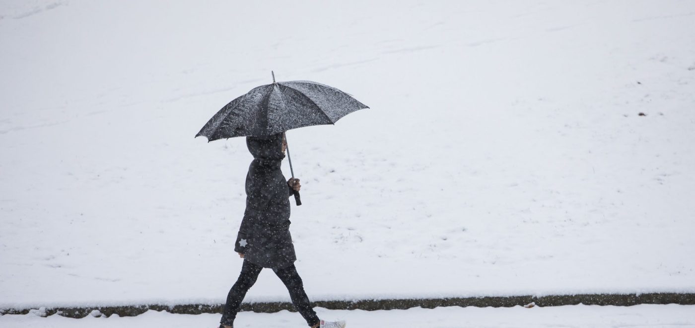 En person som går med paraply. Snø på bakken