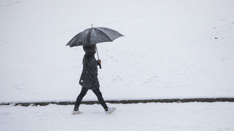 En person som går med paraply. Snø på bakken