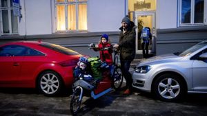 En far balanserer el-lastesykkelen mellom to parkerte biler.