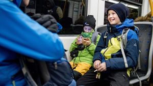 To gutter sitter på hvert sitt sete på t-banen. Smiler og ser på mobiltelefonen.