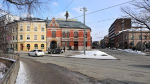 Bil kjører foran en gul og en rød bygning ved Nybrua i Oslo.