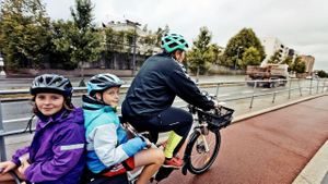 En som sykler med to barn på bagasjebrettet