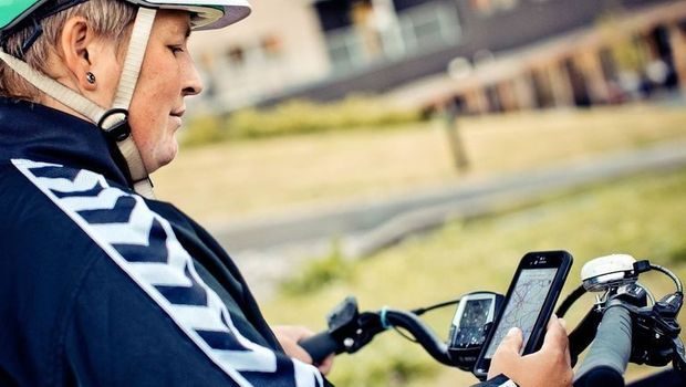 Kvinne med grønn sykkelhjelm ser på sykkelkartet på mobilen