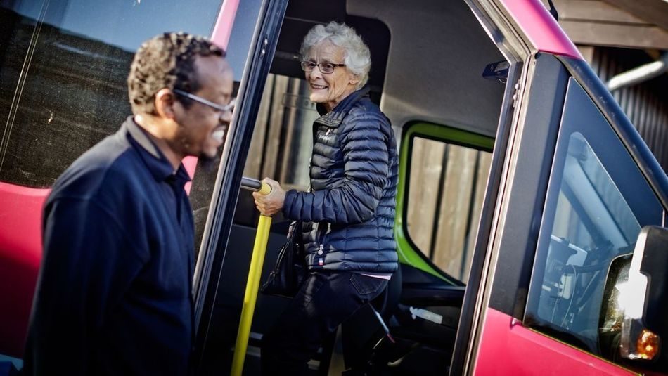 Eldre dame på vei inn i rosa buss, bussjåfør i forkant