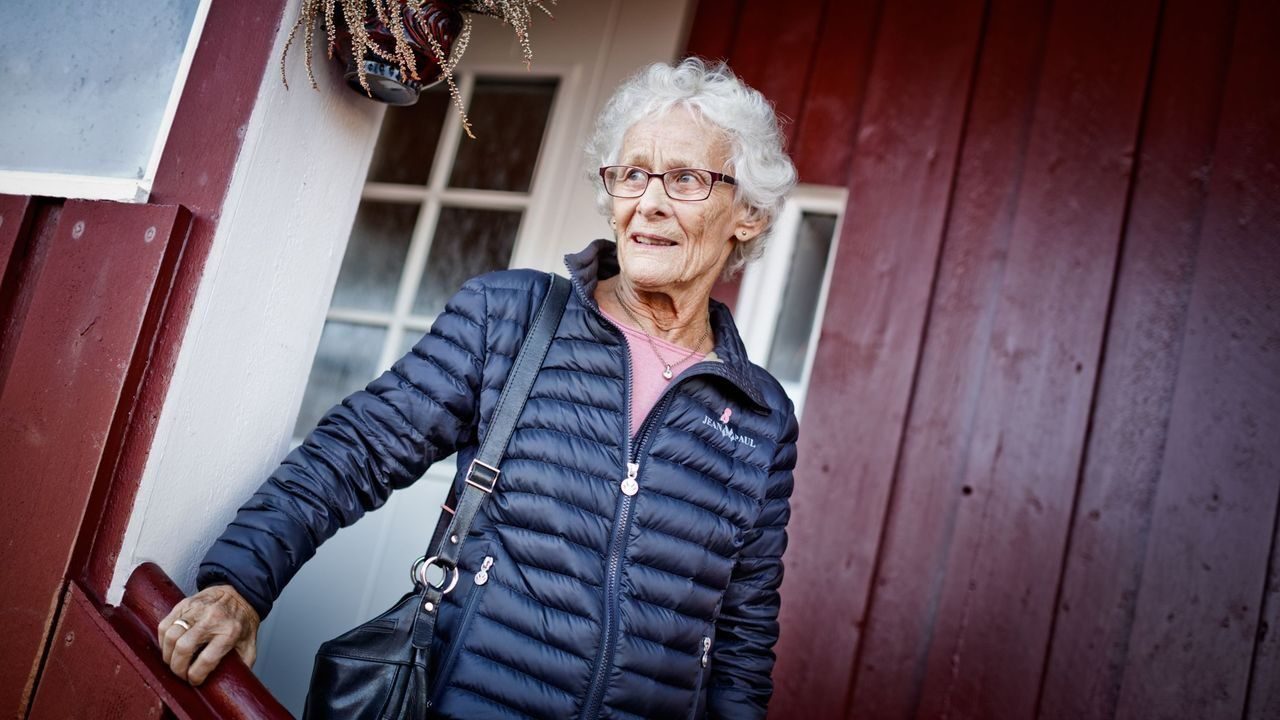 Eldre dame på utsiden av inngangsdøren til rødt hus