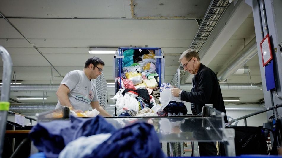 To menn sorterer klær som er levert til Fretex