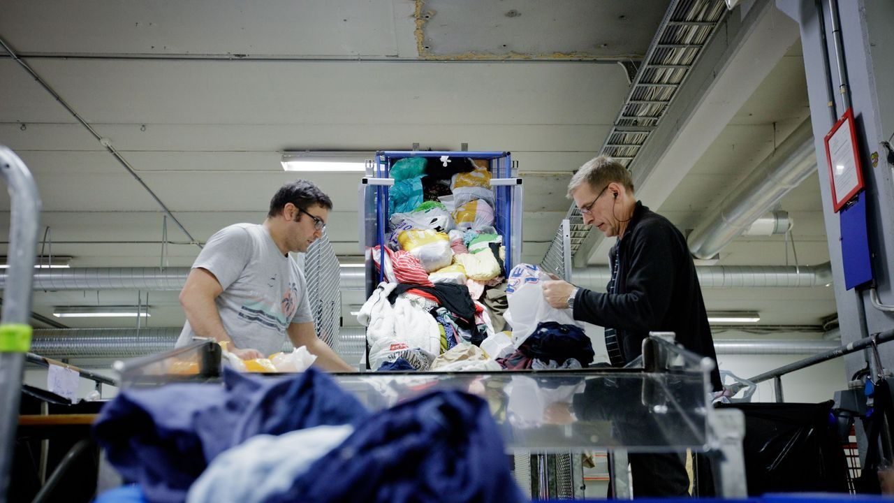 To menn sorterer klær som er levert til Fretex