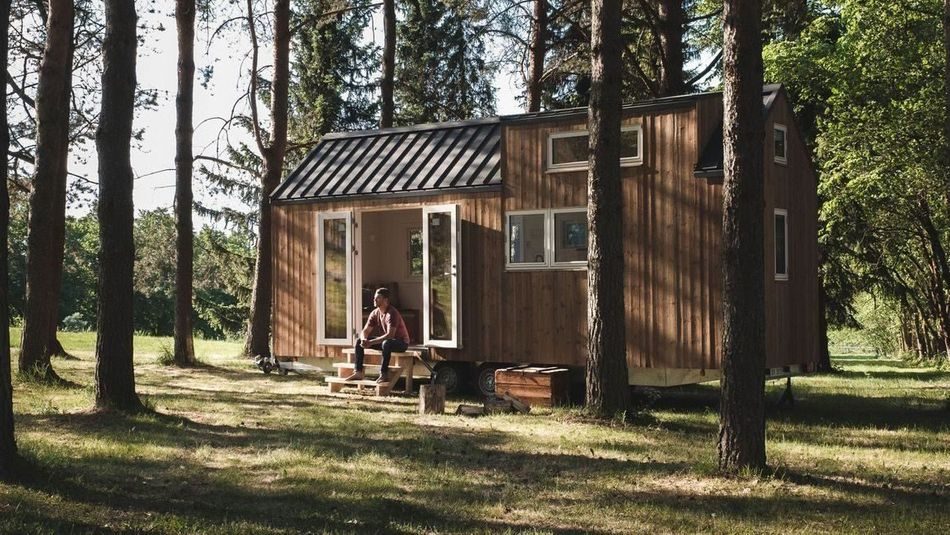 Mann sitter på trappen foran mikrohus i skogen