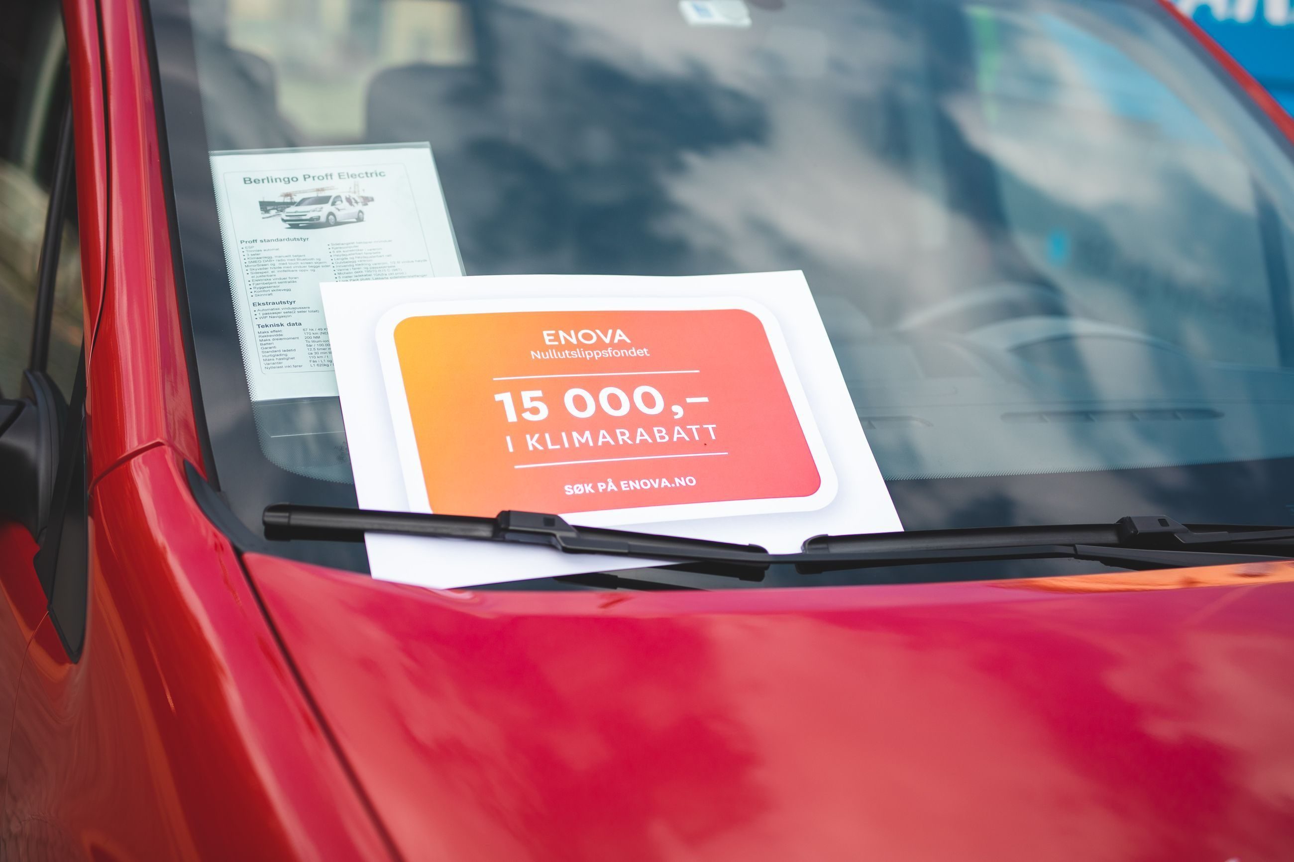 Rød bil med skilt som viser klimarabatt bak vindusviskeren på frontruta