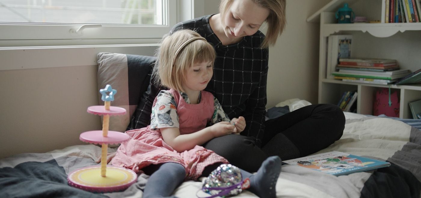En mamma sitter med datteren sin på senga og leser bok.
