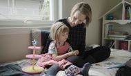 En mamma sitter med datteren sin på senga og leser bok.
