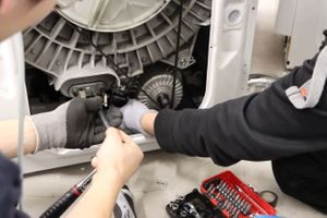 Vaskemaskin blir reparert på Hvitevareteknikk sitt verksted. To elektroteknikere skrur.