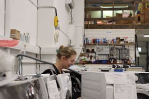 Vaskemaskin blir reparert på Hvitevareteknikk sitt verksted. To elektroteknikere skrur.